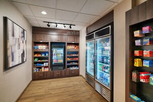 Un pasillo limpio y bien iluminado con suelo de madera, una sección refrigerada con diversas bebidas y estantes llenos de aperitivos y bebidas.