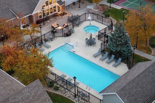 Una piscina al aire libre con sillones de descanso y zona de hidromasaje, rodeada por una valla y árboles.
