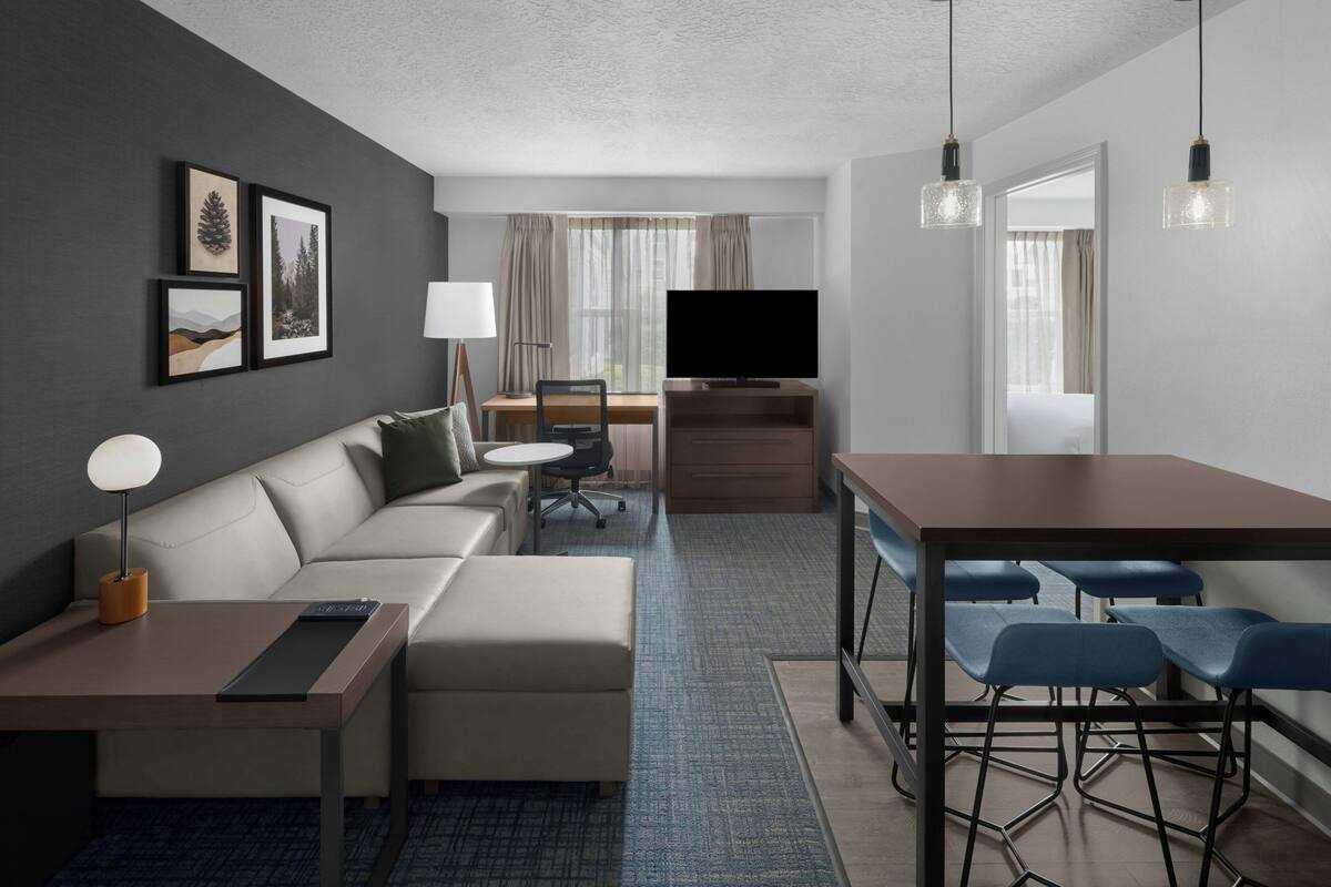 Une chambre d’hôtel moderne équipée d’un canapé, d’un bureau, d’une télévision et d’un coin repas avec des chaises.