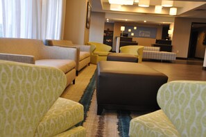 Vestíbulo de hotel con arreglos de asientos, un mostrador de recepción y una alfombra estampada.