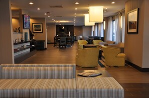 A hotel lobby with a reception desk, seating area, and a dining space.
