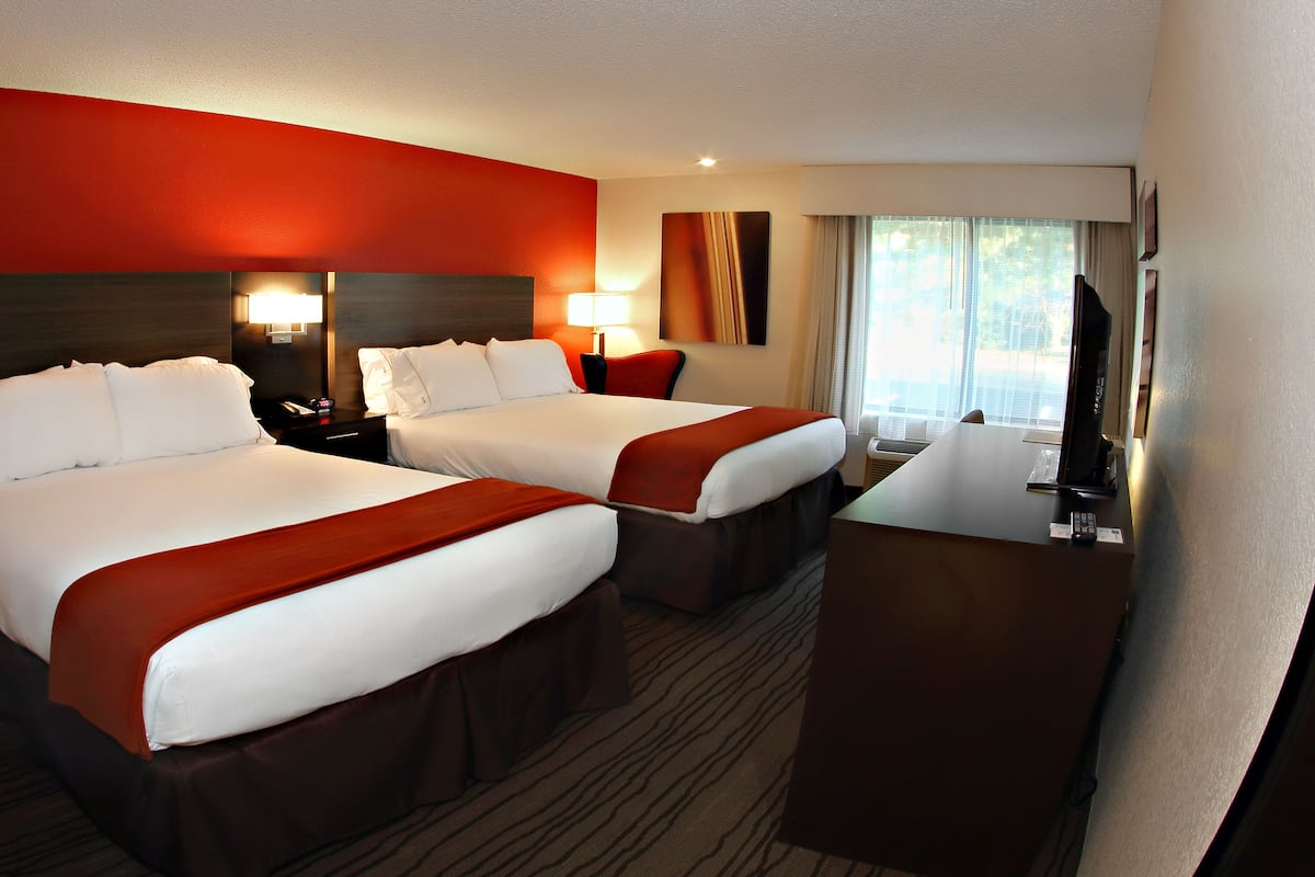 A hotel room with two beds, a desk, a TV, and a window with curtains.