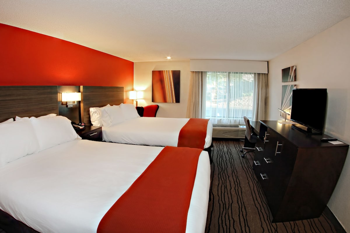 A hotel room with two beds, a TV, a desk, and a window with curtains.