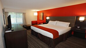 A hotel room with a large bed, a desk with a TV, a red armchair, and a nightstand with a lamp. - Holiday Inn Express Brentwood South - Cool Springs by IHG (Brentwood)