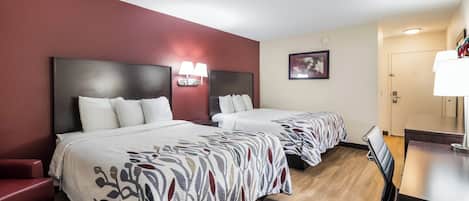 Ein Hotelzimmer mit zwei Betten, einem Schreibtisch, einem Sessel, einem roten Sofa und einer Wandleuchte.