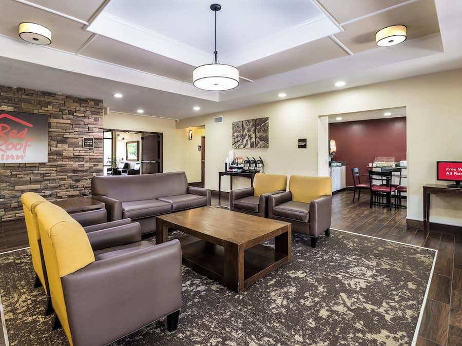Um hall de hotel com balcão de recepção, área de estar com sofás e cadeiras, um espaço para café e uma tela de televisão anunciando Wi-Fi gratuito.