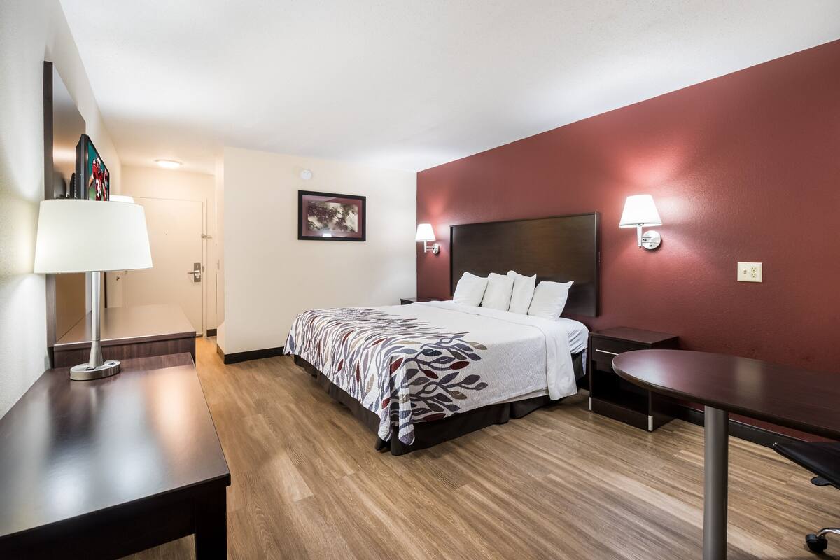 A hotel room with a bed, bedside tables, a desk, and a lamp.