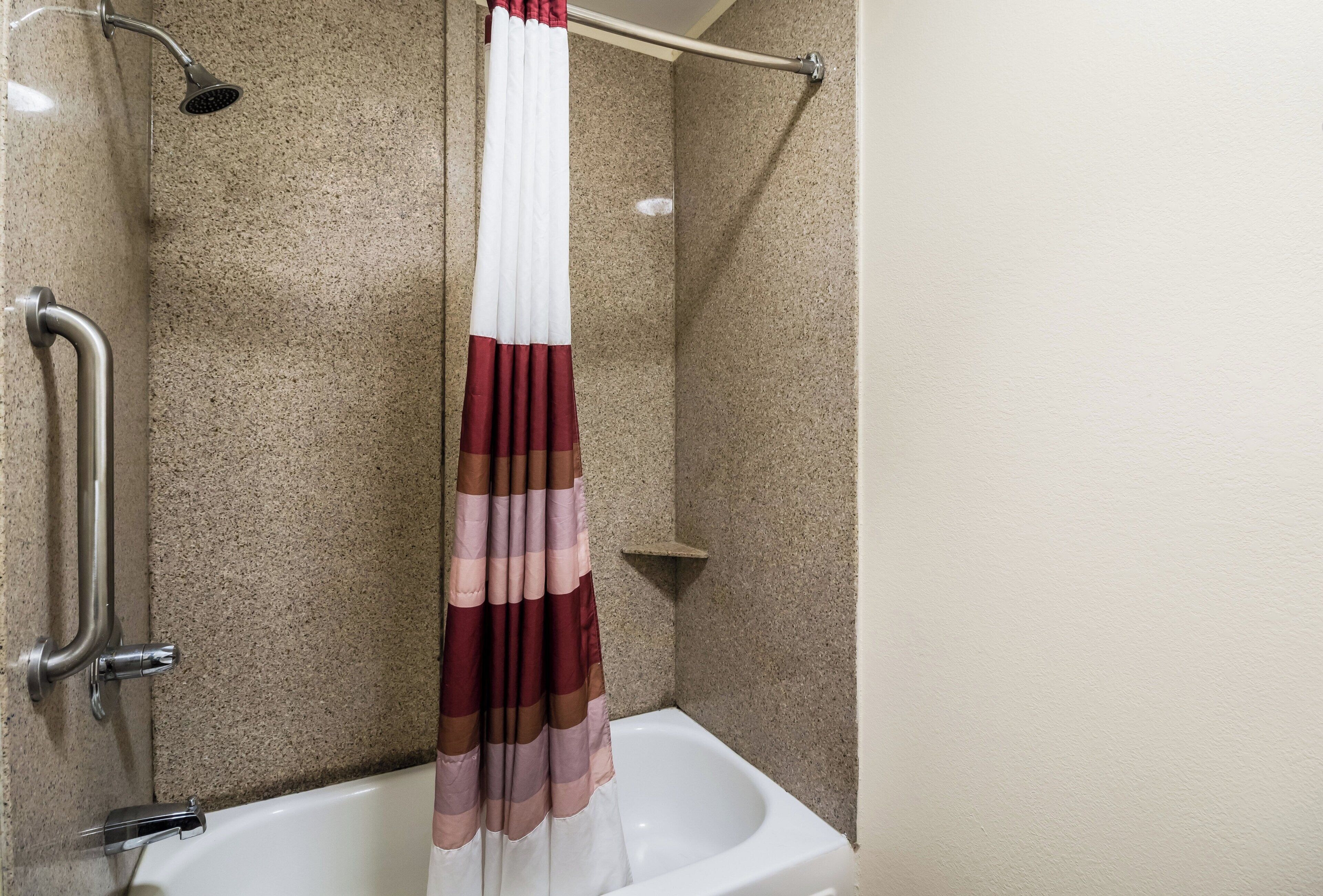 Un baño con ducha, barra de apoyo y bañera.