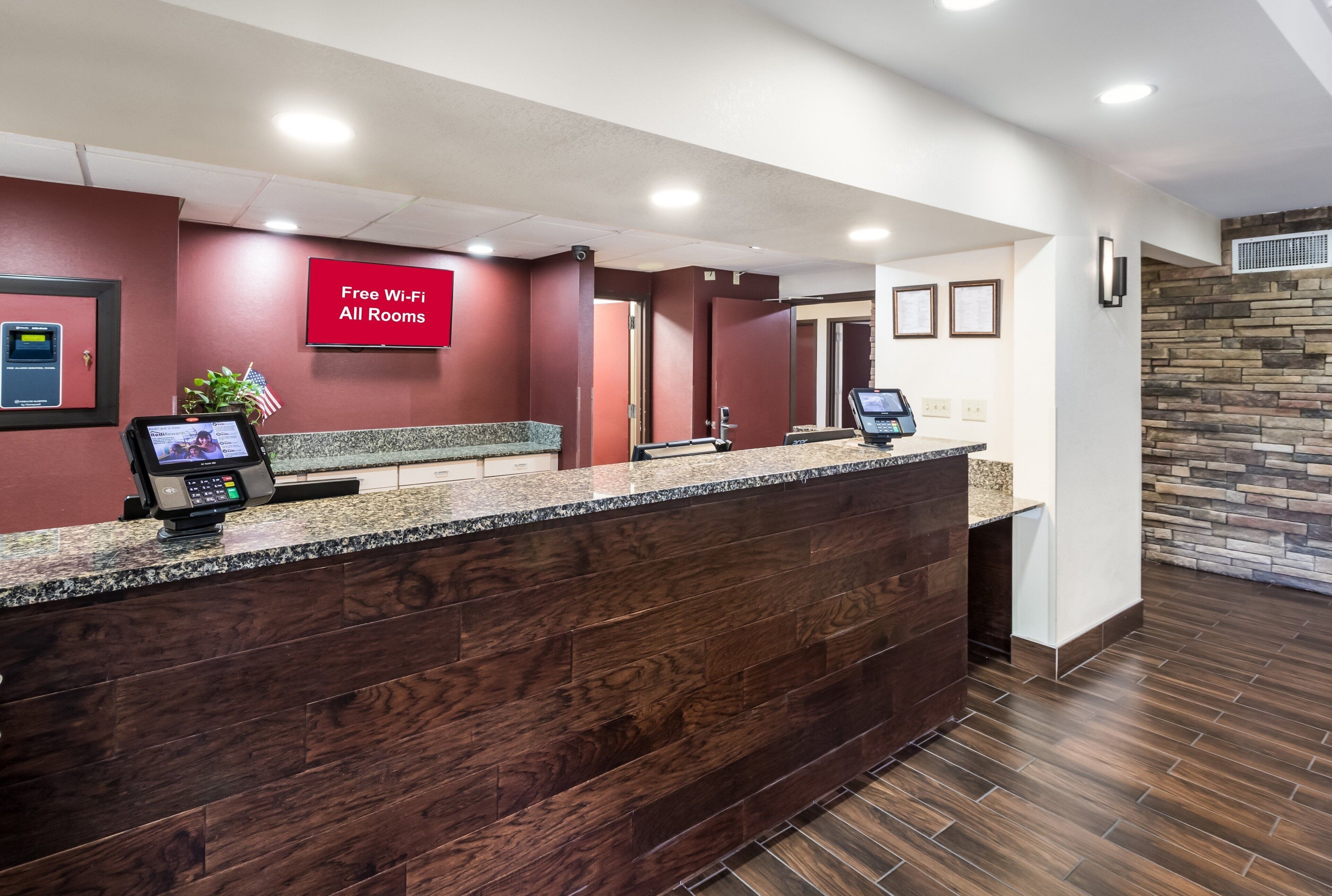 A hotel reception area with a wooden reception desk, a digital display, and a sign indicating free Wi-Fi in all rooms.
