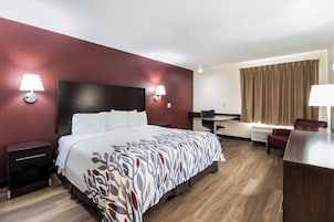 Habitación de hotel con una cama grande, dos lámparas de noche, un escritorio, una silla y una ventana con cortinas.