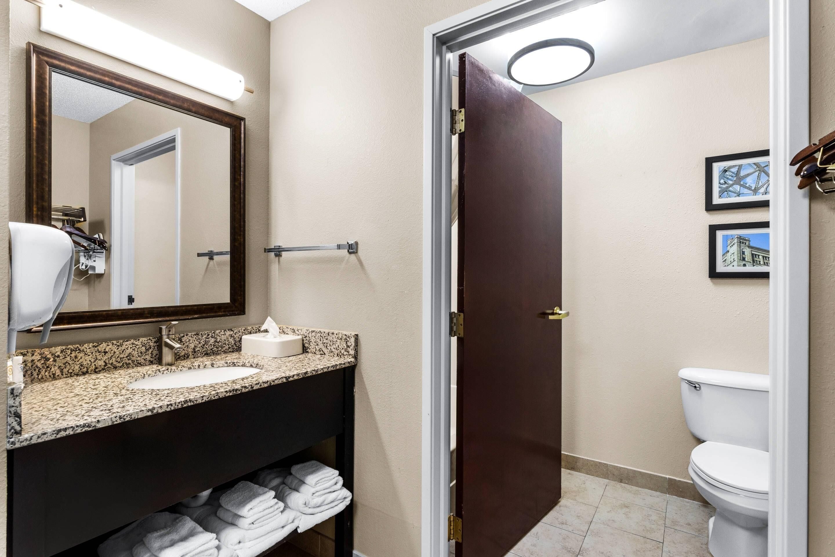 A bathroom with a sink, mirror, towel rack, toilet, and framed pictures on the wall.