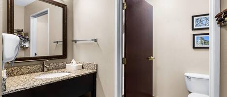 A bathroom with a sink, mirror, towel rack, toilet, and framed pictures on the wall.