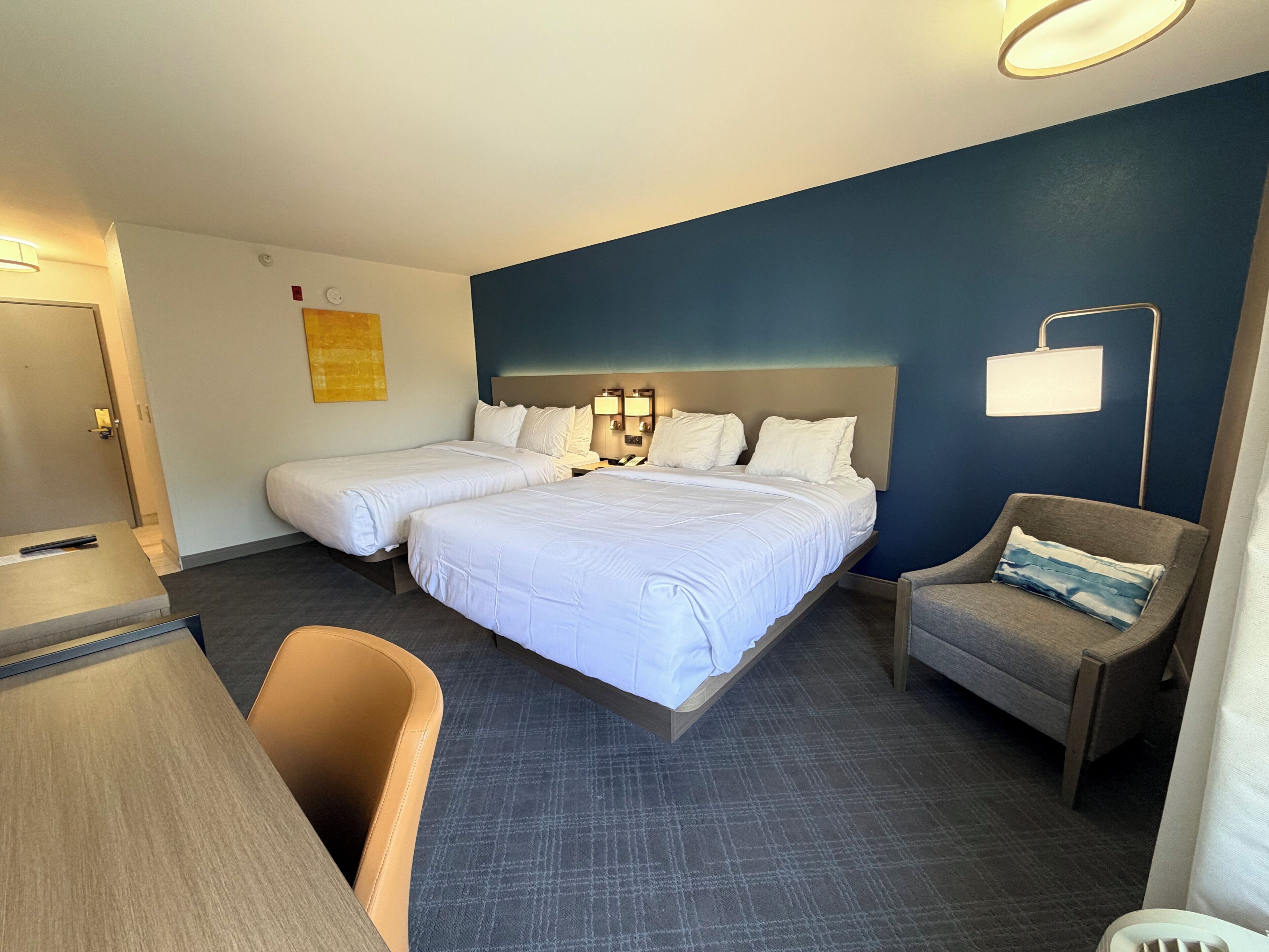 Habitación de hotel con dos camas, un escritorio, una silla y una mesita de noche.