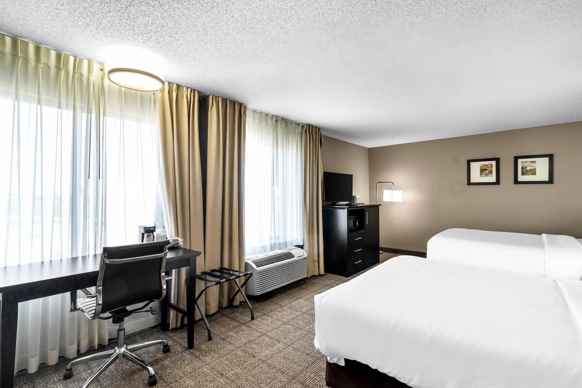 A hotel room with a desk, chair, two beds, a TV, and a heater.