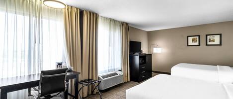 Habitación de hotel con escritorio, silla, dos camas, televisor y calefactor.