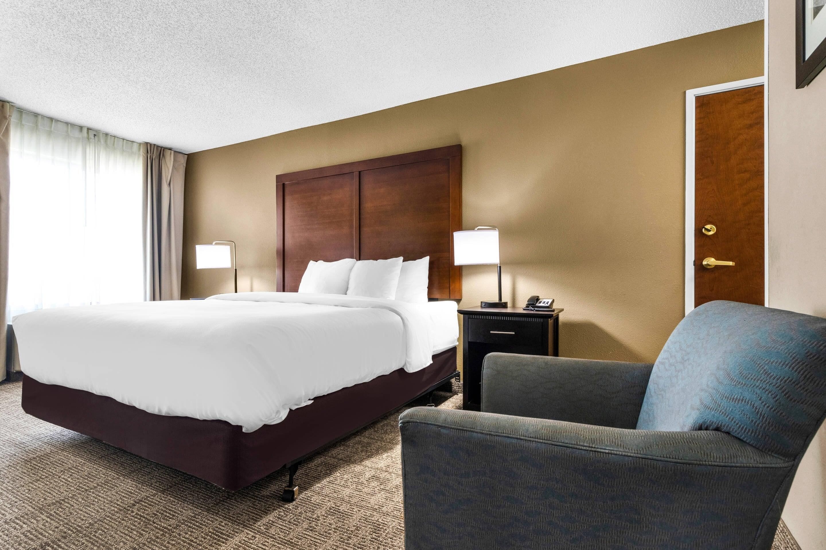 Une chambre d’hôtel avec un grand lit, une chaise, une table de chevet et une porte.