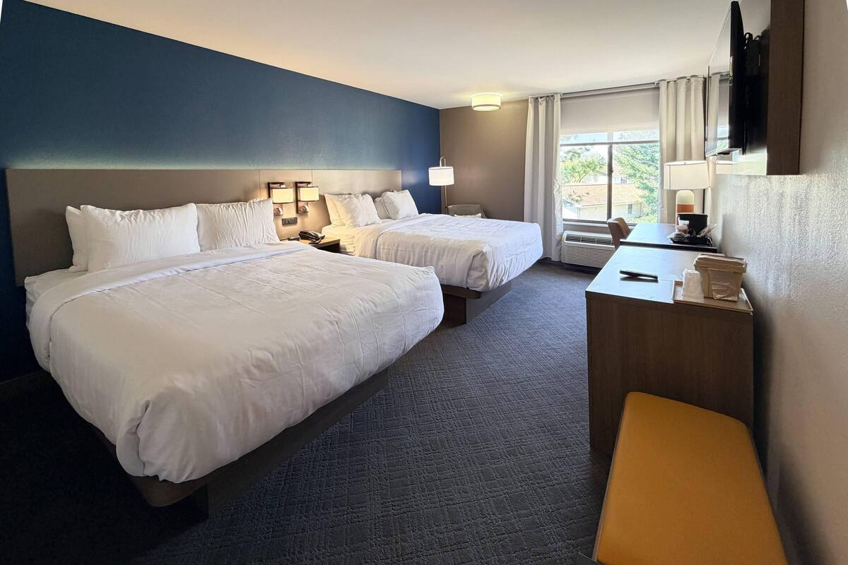 A hotel room with two beds, a desk, a chair, a TV, and a window with curtains.