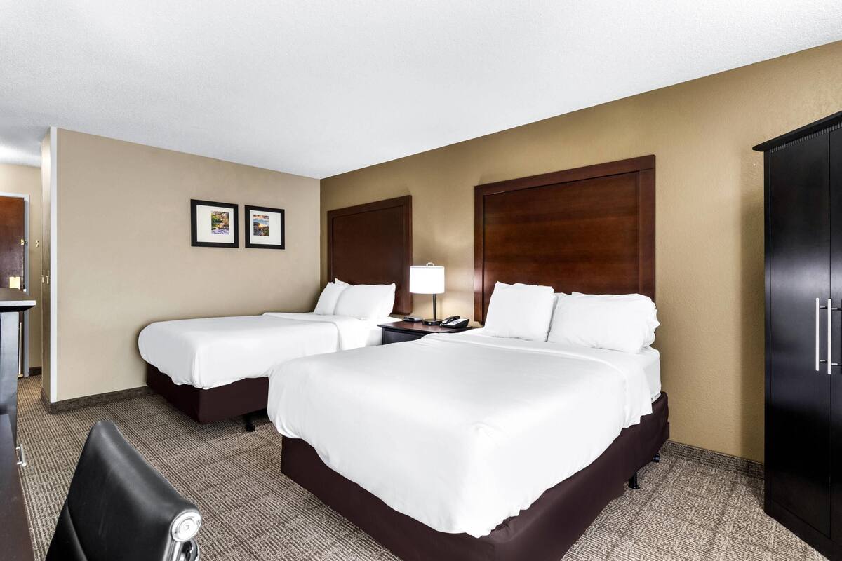 A hotel room with two beds, a desk, a chair, a wardrobe, and a lamp.