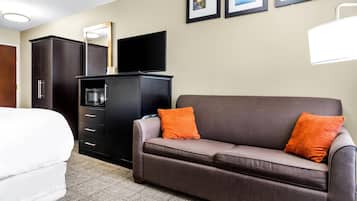 Une chambre d’hôtel comprenant un lit, un canapé, une télévision, une machine à café, une armoire et des tableaux encadrés accrochés au mur.
