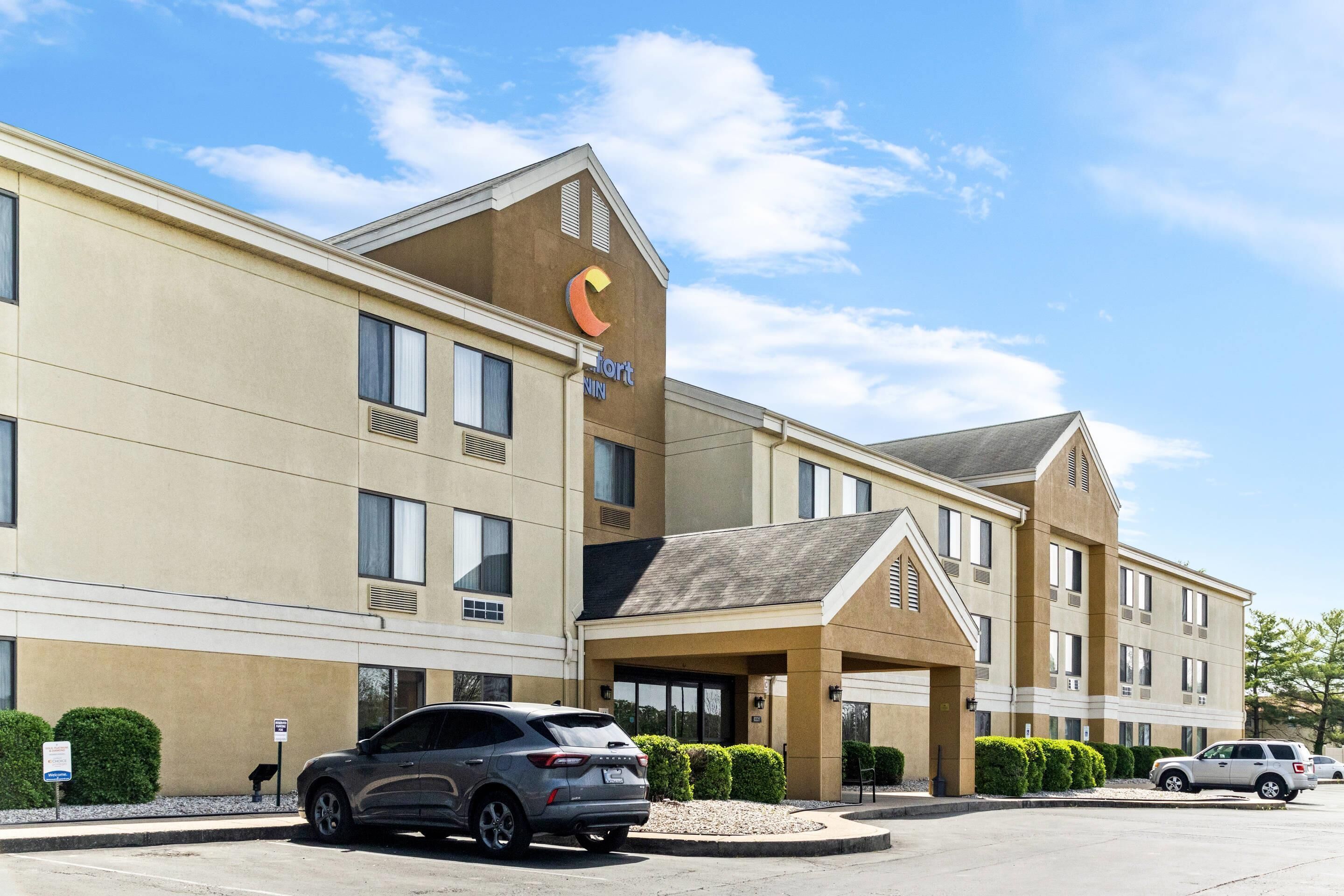 A hotel with a prominent logo, multiple windows, and a parking lot with cars.