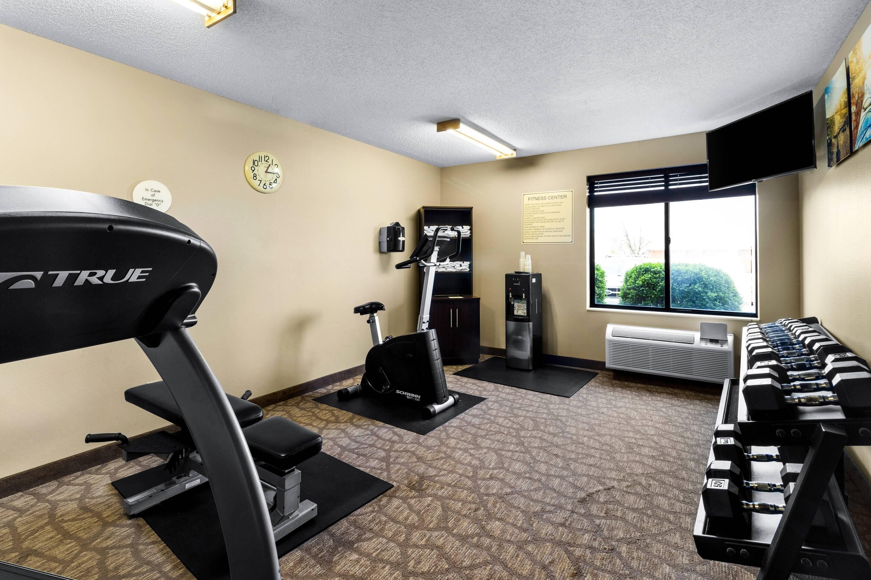 Un gimnasio con cinta de correr, elíptica y mancuernas.