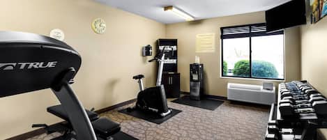 A fitness center with a treadmill, elliptical, and dumbbells.