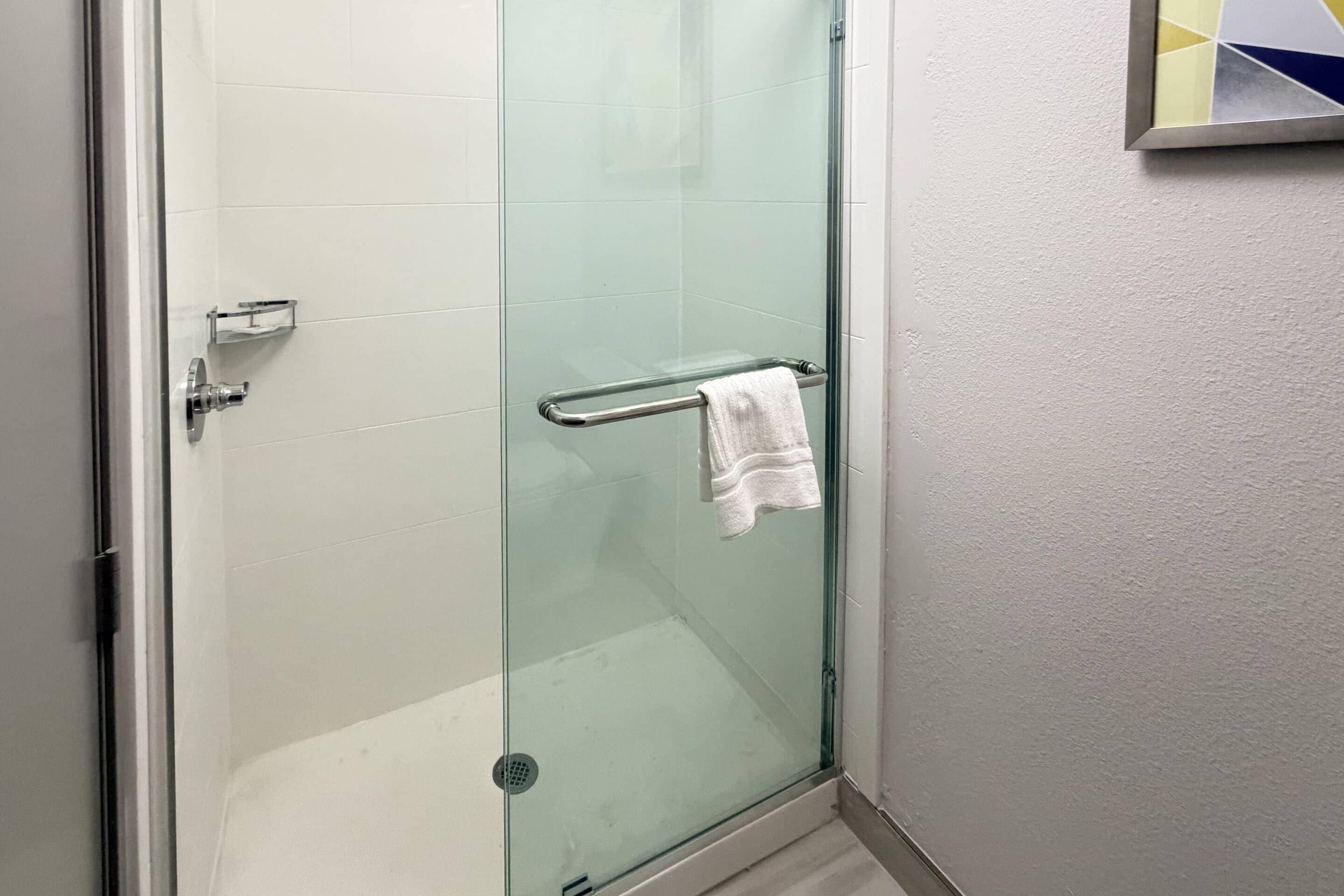 A glass-enclosed shower with a towel rack and a small shelf.