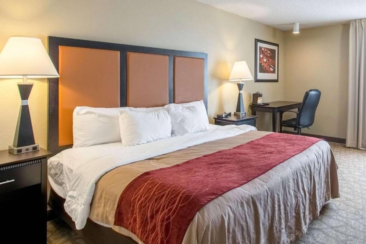 A hotel room with a bed, two bedside tables, a desk, a chair, and a lamp.