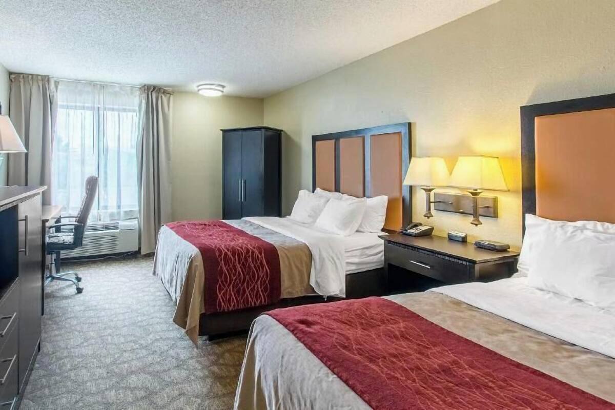A hotel room with two beds, a desk, a chair, a wardrobe, and a nightstand with lamps.