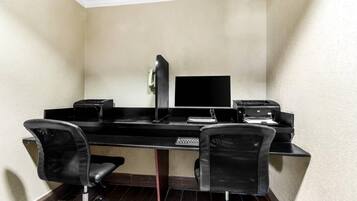 A corner office with a desk, two chairs, a computer monitor, a printer, and a telephone.