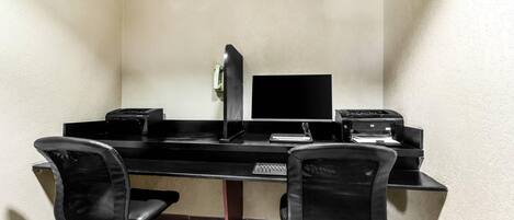 A corner office with a desk, two chairs, a computer monitor, a printer, and a telephone.