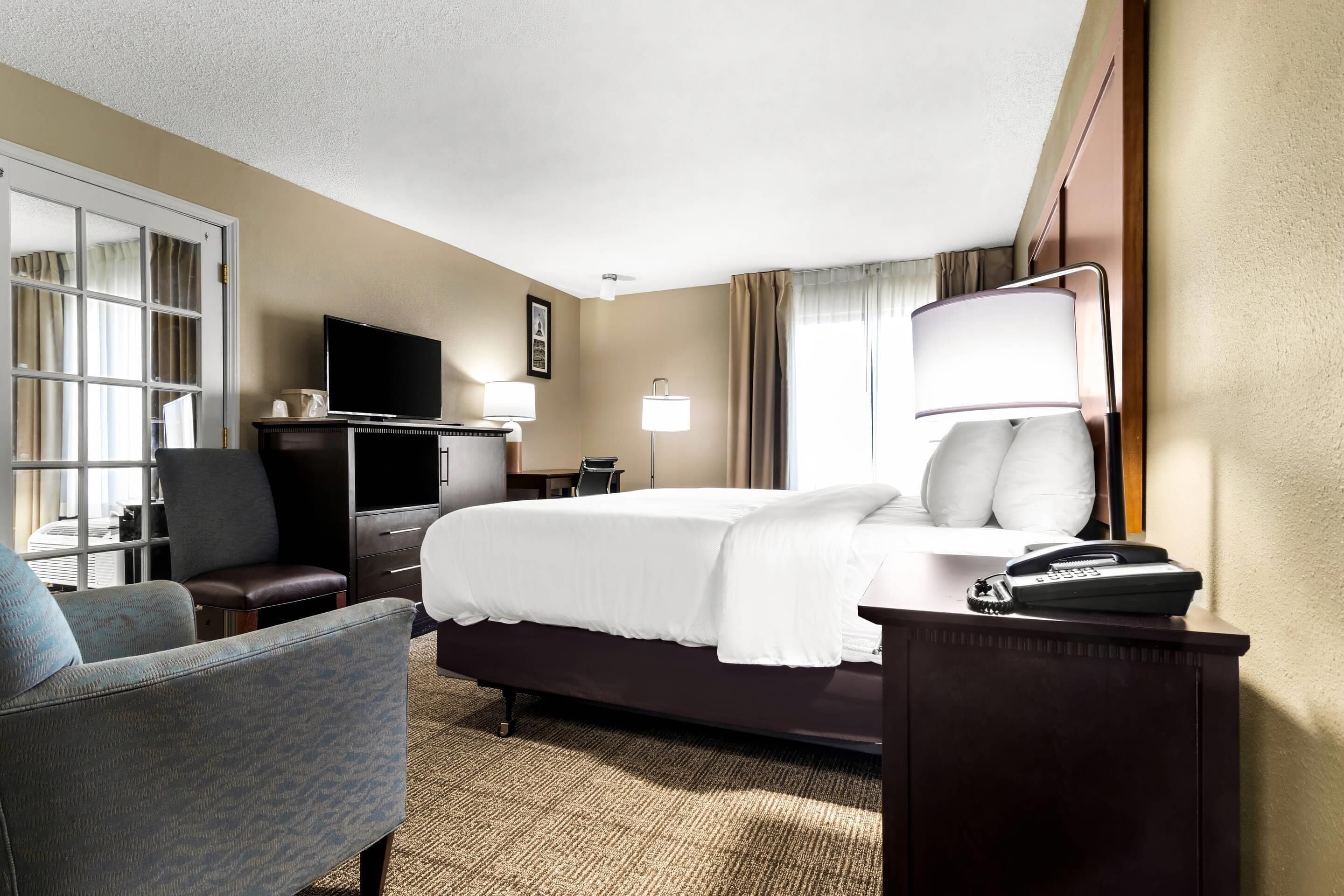 A hotel room with a bed, a desk with a telephone, a chair, a television, and a window with curtains.