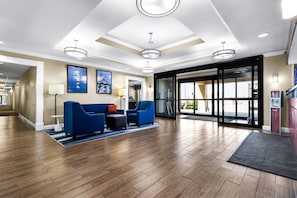 Eine Hotelhalle mit einer Rezeption, einem blauen Sitzbereich, Holzböden und großen Fenstern.
