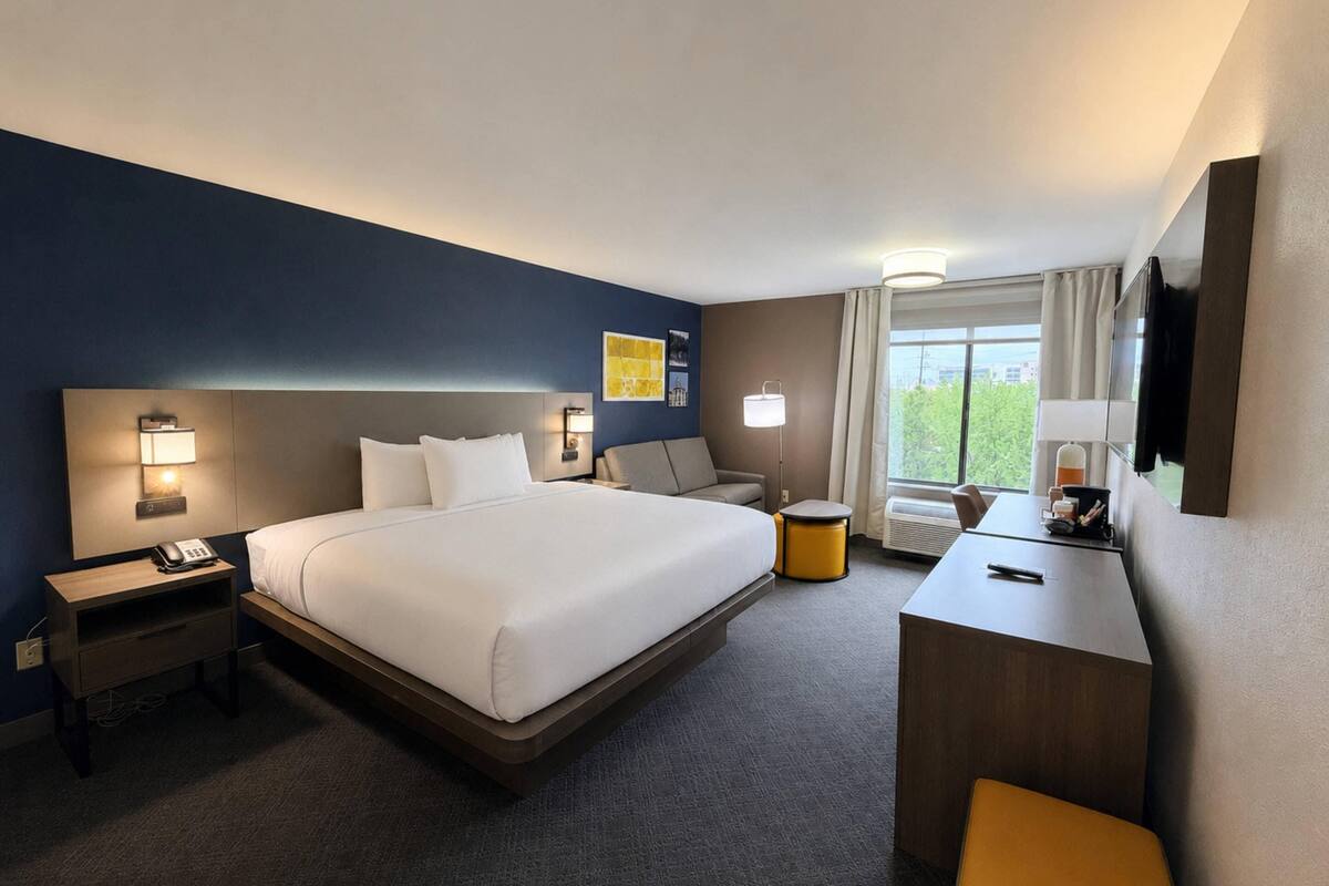 A hotel room with a large bed, bedside tables, a desk, a chair, and a window with curtains.