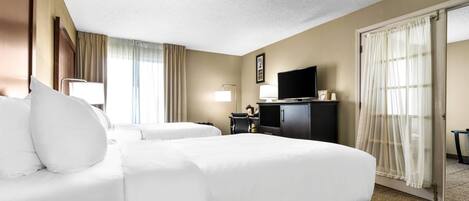A hotel room with two beds, a desk, a television, and a door with curtains.