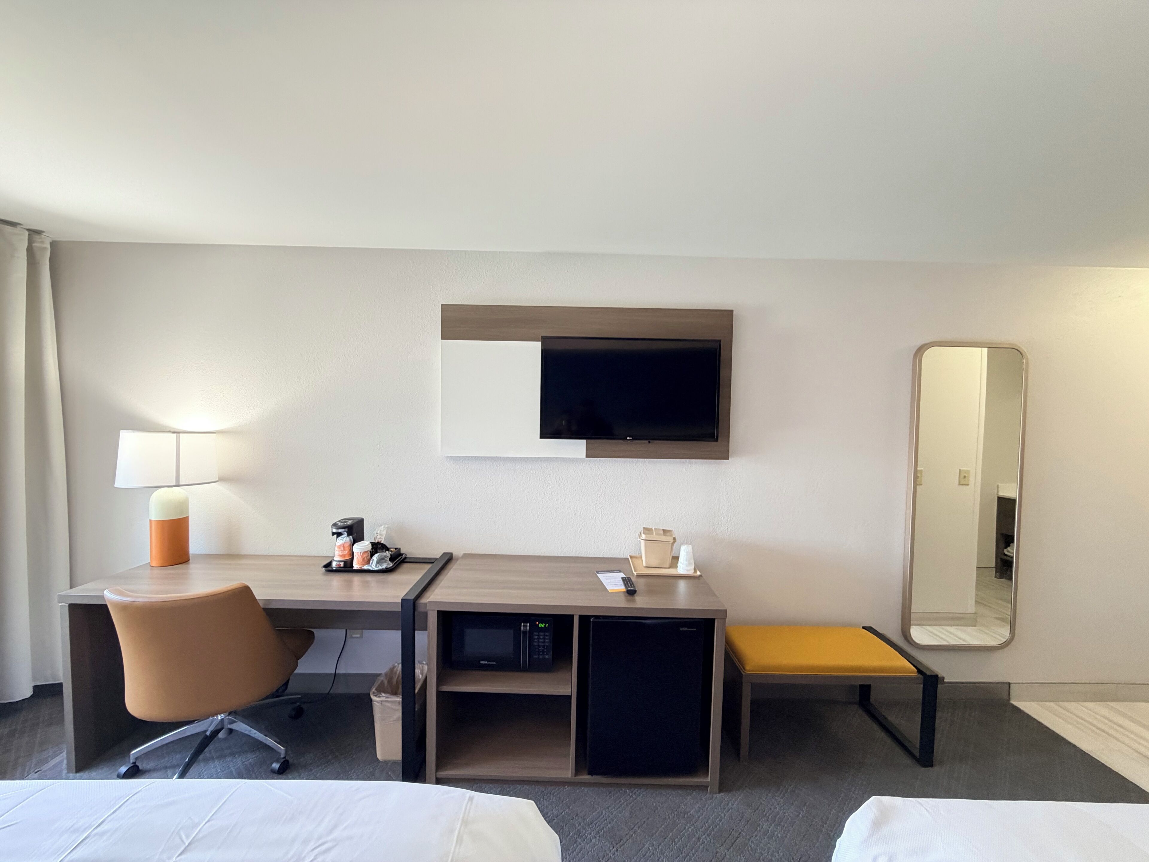 Une chambre d’hôtel équipée d’un bureau, d’une chaise, d’un lit, d’une télévision et d’un miroir.