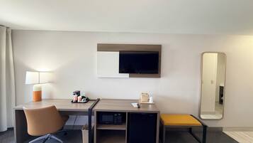 Une chambre d’hôtel équipée d’un bureau, d’une chaise, d’un lit, d’une télévision et d’un miroir.