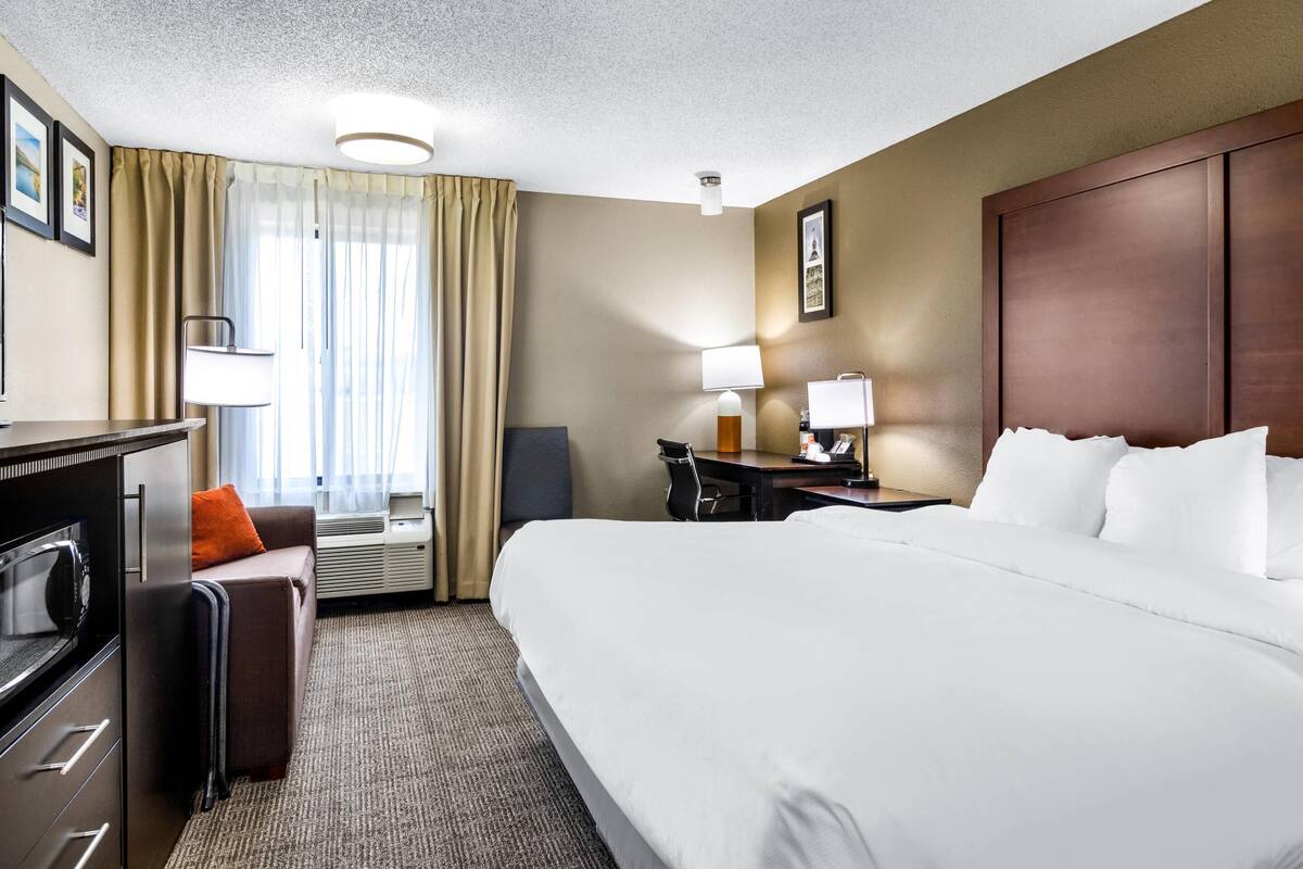 A hotel room with a bed, a desk, a chair, a desk lamp, a television, and a window with curtains.