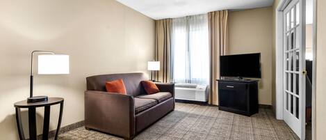 Una habitación de hotel con sofá, televisión, lámpara y ventana con cortinas.