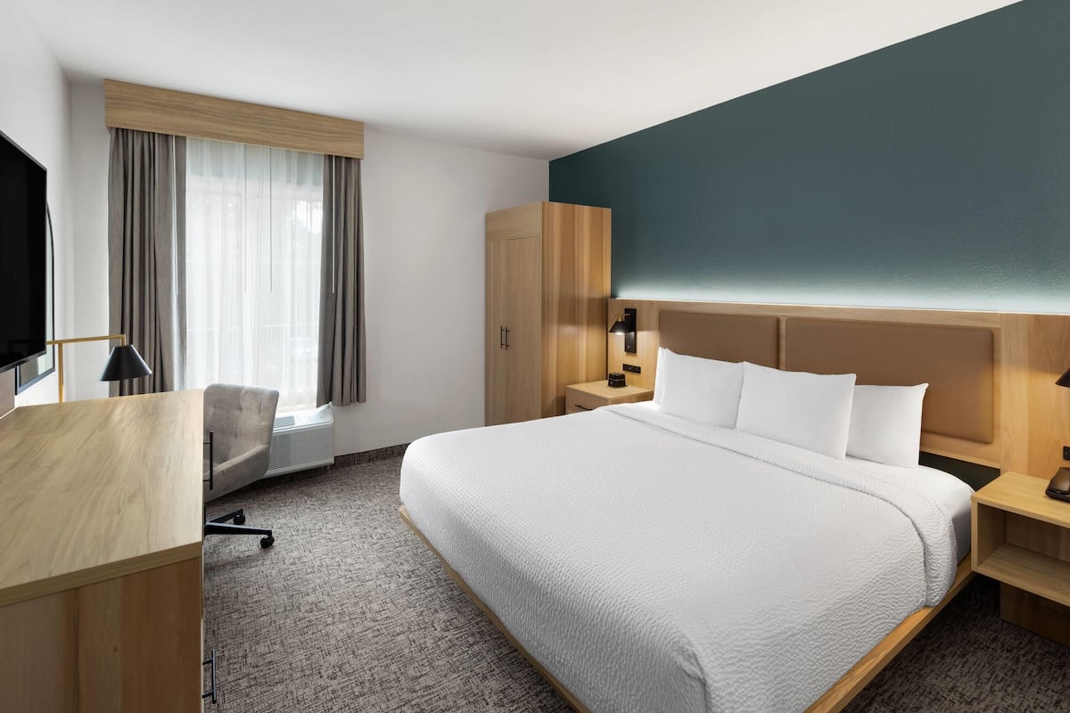 Une chambre d’hôtel avec un grand lit, un bureau, une chaise, une armoire et un téléviseur.