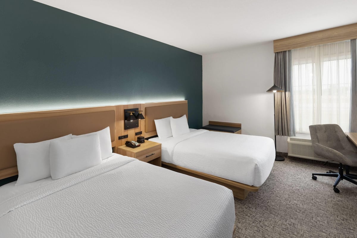 Une chambre d’hôtel avec deux lits, un bureau, une chaise et une fenêtre avec des rideaux.