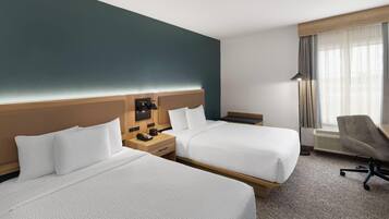 Une chambre d’hôtel avec deux lits, un bureau, une chaise et une fenêtre avec des rideaux.