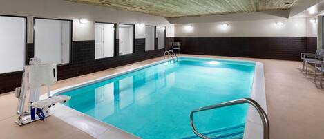 An indoor swimming pool with clear blue water, a ladder, and a lifeguard chair.
