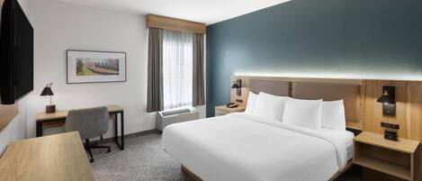 A hotel room with a large bed, a desk, a chair, a nightstand, a lamp, and a picture on the wall.