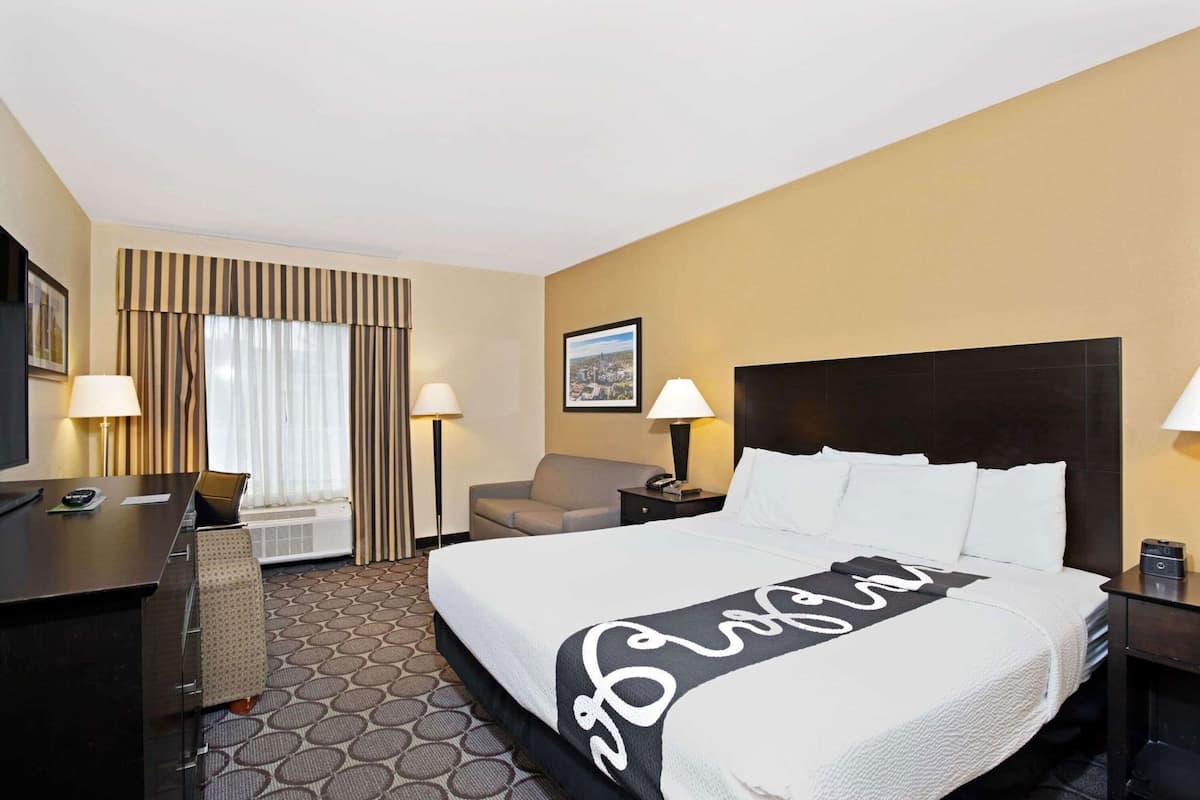 Une chambre d’hôtel avec un lit, un bureau, une chaise, un canapé, une lampe et un tableau au mur.