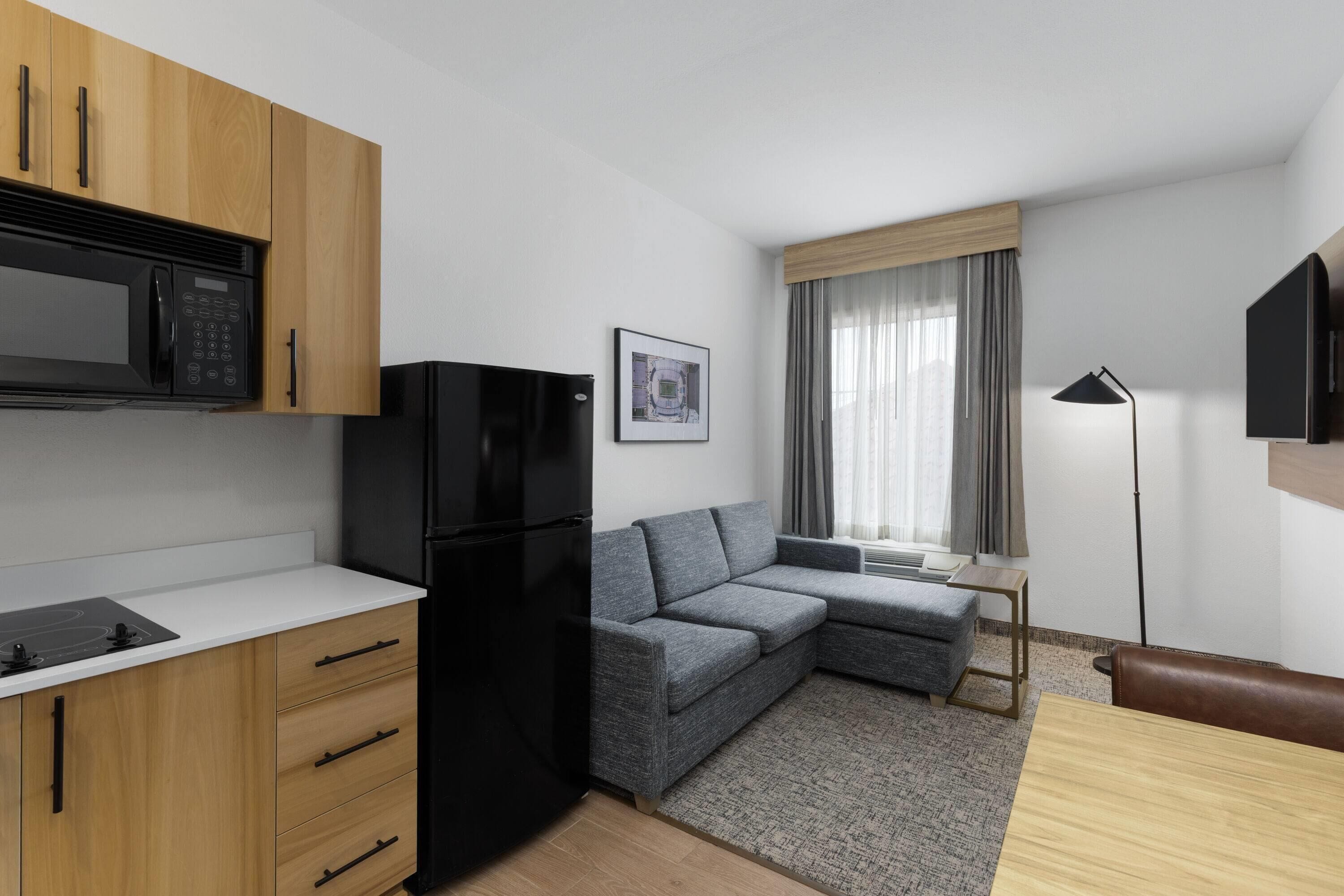 A compact living space with a kitchenette, a gray sofa, a small table, and a TV mounted on the wall.