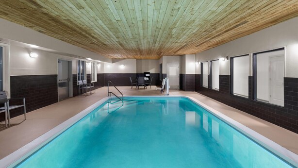 Una piscina interior con techo de madera, paredes de azulejos y un área de estar con sillas y una mesa.