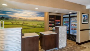 Zona de recepción con un mural de paisaje campestre, un mostrador y vitrinas refrigeradas con aperitivos.