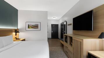 Una habitación de hotel moderna con una cama grande, un televisor de pantalla plana montado en la pared, un aparador de madera y un cuadro enmarcado.