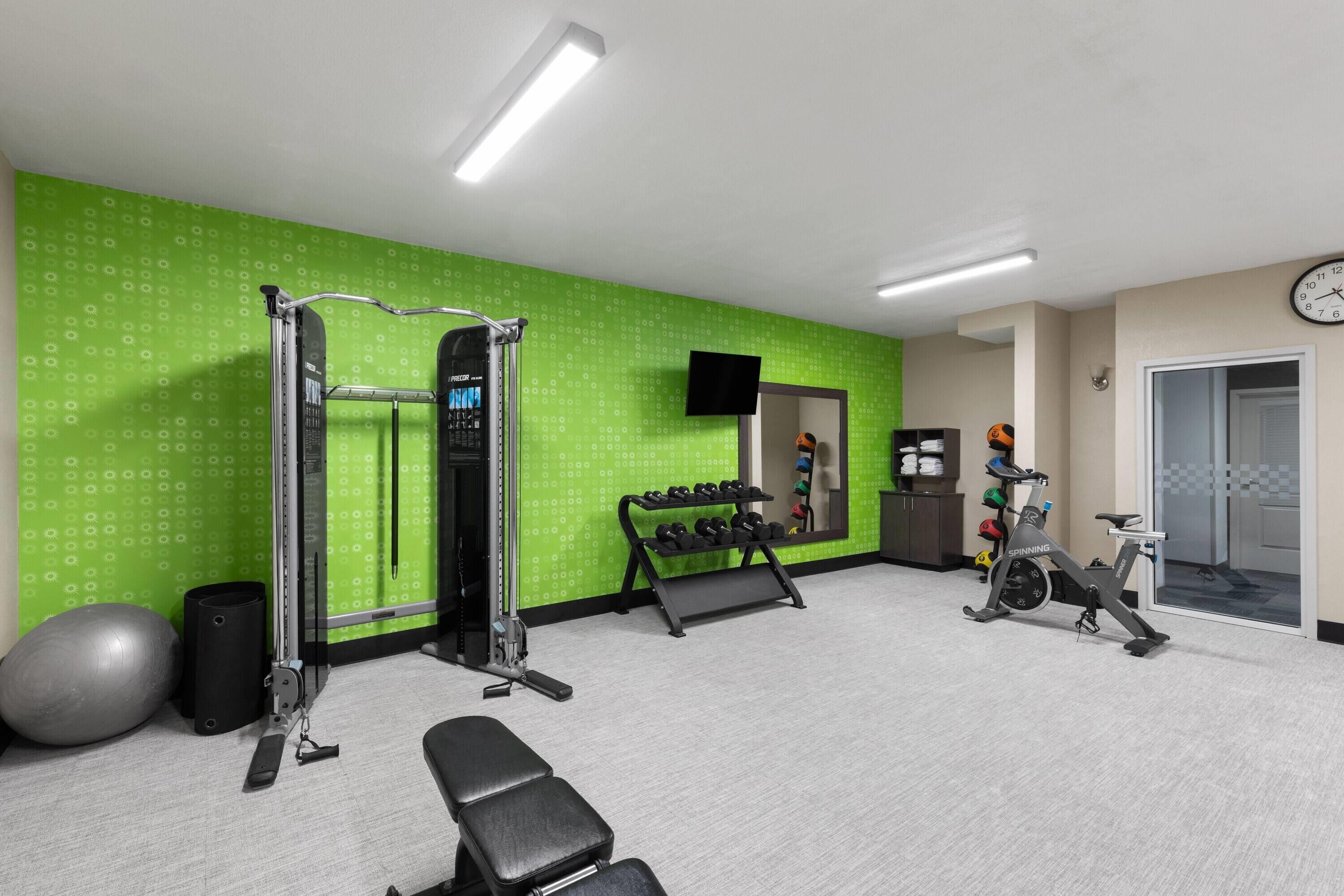 A gym with exercise equipment, a wall-mounted TV, and a clock.